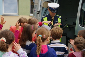 Policjant z wydziału ruchu drogowego rozdaje dzieciom opaski odblaskowe