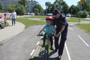 Policjant pomaga utrzymać równowagę jadącemu na rowerze dziecku