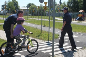 Policjant i dziecko jadące na rowerze ustępują pierwszeństwa policjantce przechodzącej przez przejście dla pieszych