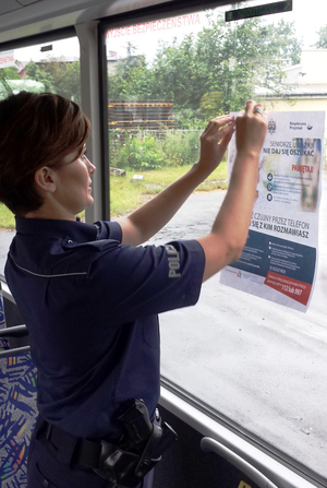 Policjantka umieszcza na szybie autobusu plakat