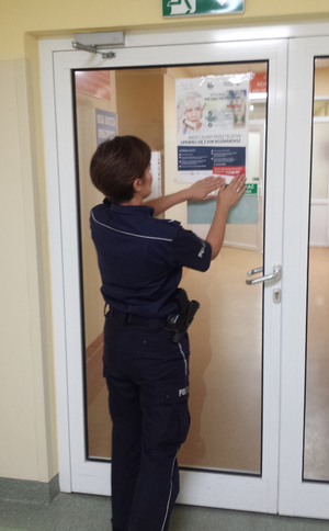 Policjantka umieszcza plakat na drzwiach