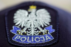 Na zdjęciu widoczna częściowo policyjna czapka z naszywką przedstawiającą białego orła w koronie, pod którym widnieje niebieska wstęga z napisem POLICJA.