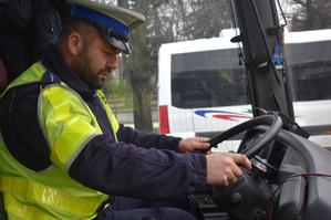 Na zdjęciu widoczny policjant siedzący za kierownicą autokaru.