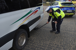 Na zdjęciu widoczny policjant sprawdzający podwozie busa.