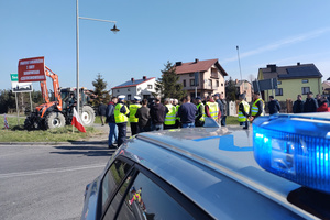 Na zdjęciu widoczny częściowo radiowóz, umundurowani policjanci oraz osoby biorące udział w zgromadzeniu.
