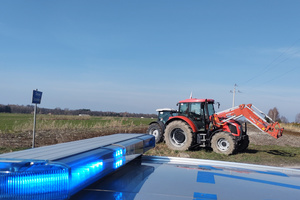 Na zdjęciu widoczny częściowo radiowóz oraz ciągnik rolniczy ustawiony na poboczu.