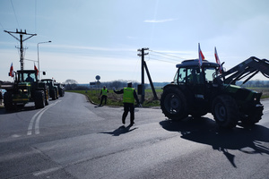 Na zdjęciu widoczny umundurowany policjant oraz ciągniki rolnicze ustawione na jezdni.