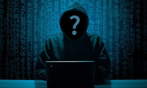 Grafika przedstawiająca postać w kapturze ze znakiem zapytania w miejscu twarzy. Postać siedzi przed laptopem.